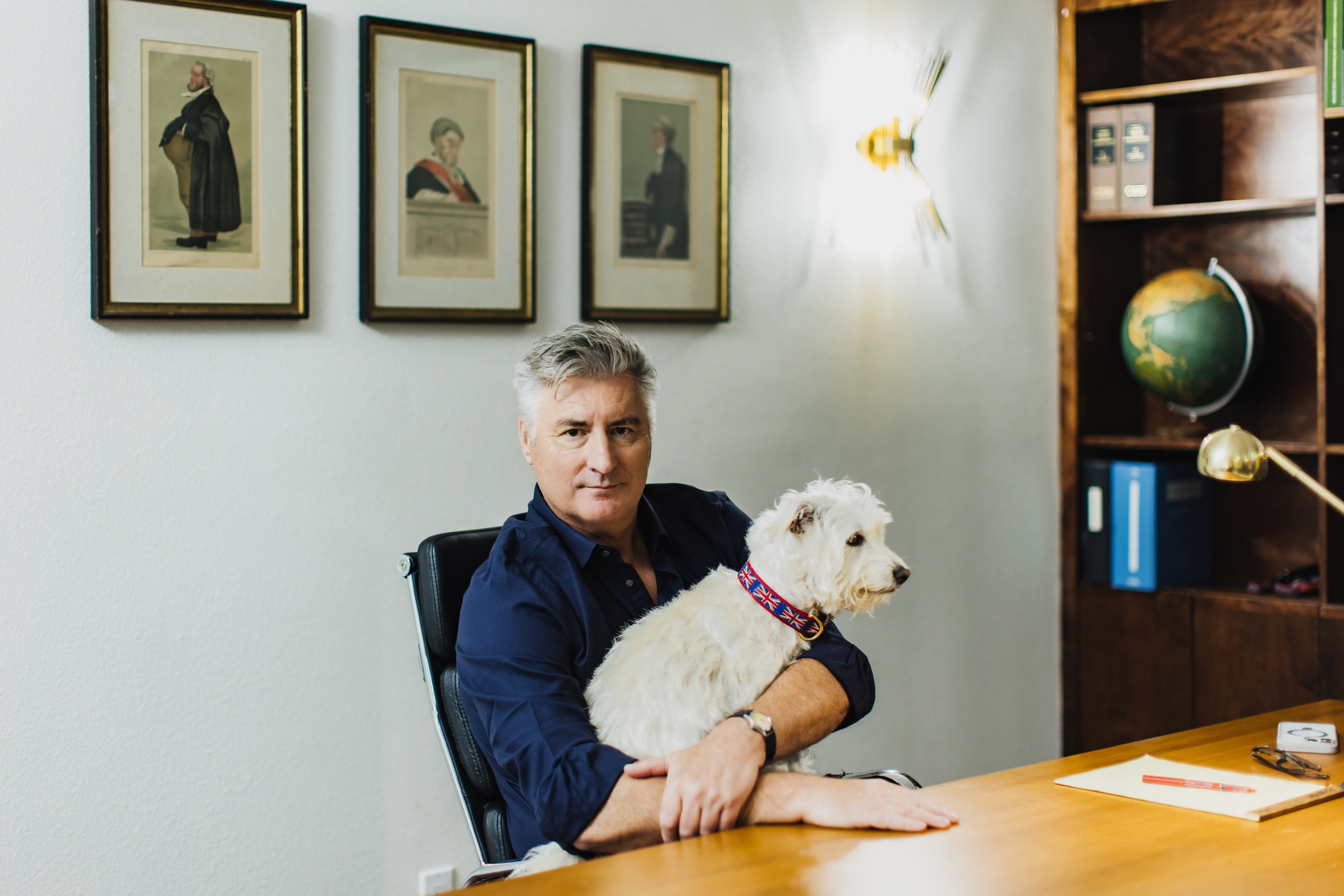 A portrait of a man holding his dog in his office